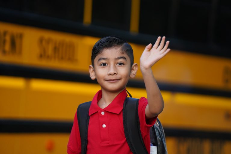 student waiving in front of a school bus